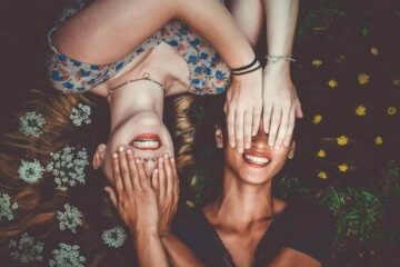 Two women smiling with hands on faces, promoting fashion and confidence