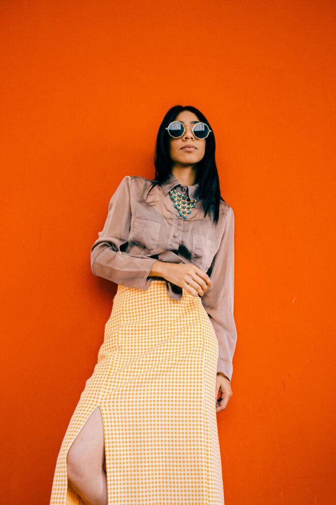 Fashionable Woman in Sunglasses Posing Against Orange Wall