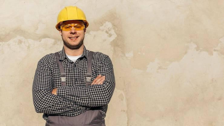 A construction worker in a yellow hard hat and safety glasses
