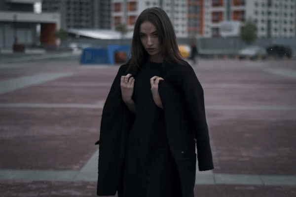 Woman in parking lot with coat under moon-themed sky