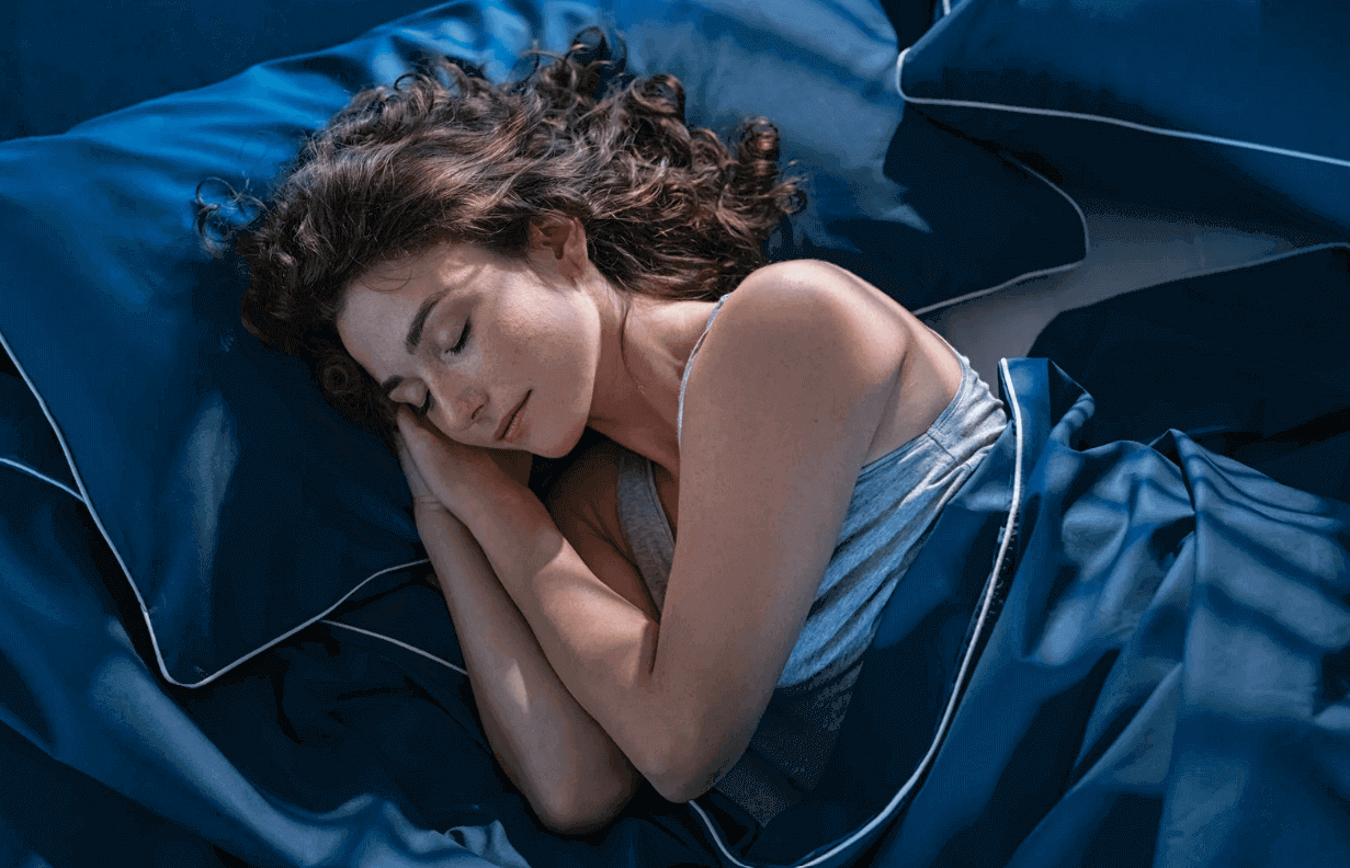 Woman sleeping in bed with blue sheets for detox-friendly routine