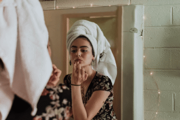 Woman with towel on head looking in mirror reflecting on beauty enhancements